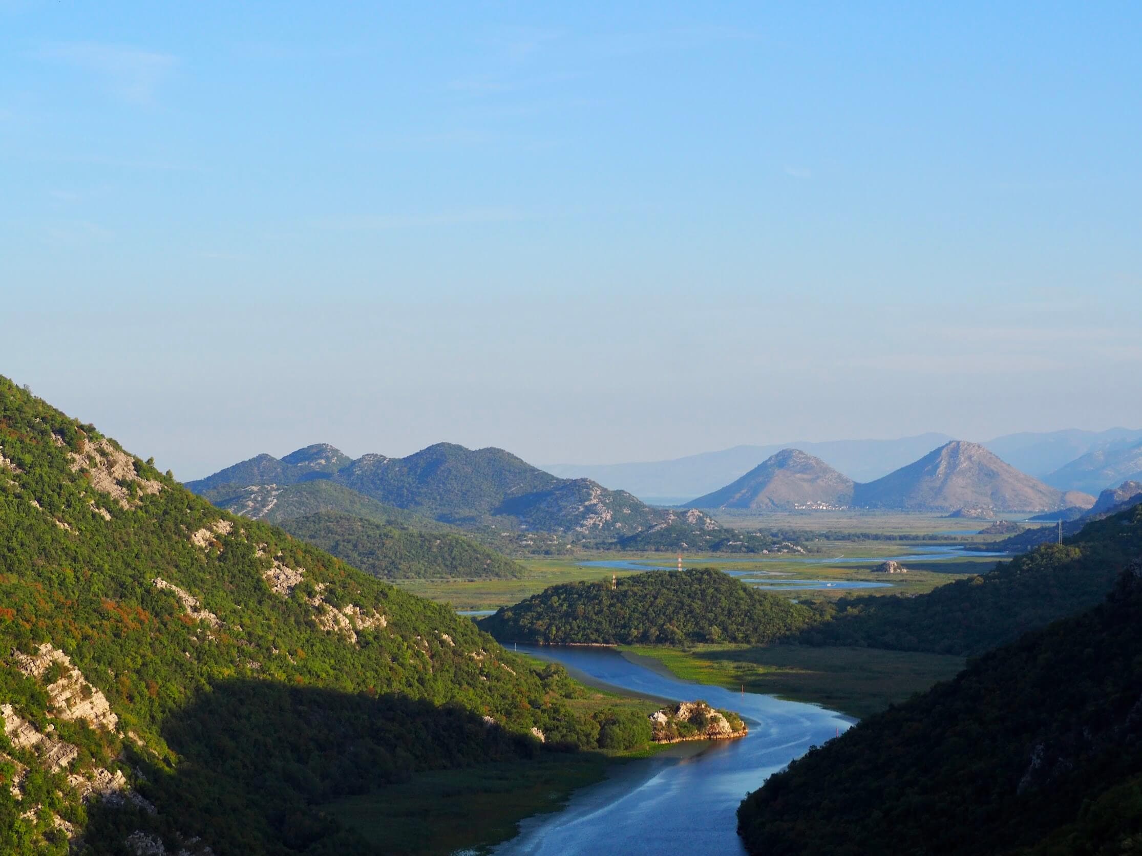 Forested hill mirrored in the still water of Lake Skadar, Montenegro